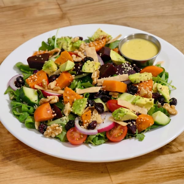 Colorful salad with avocado, beets, sweet potato, walnuts, and dressing on a white plate.