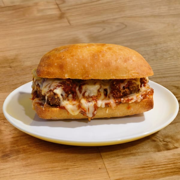 A meatball sub sandwich with melted cheese and marinara sauce on a white plate.